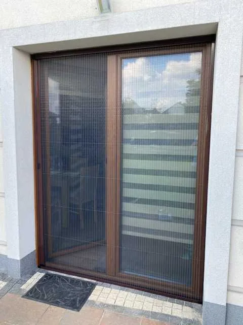 Moskitiera plisowana w profilu drewnopodobnym w realizacji na Śląsku - ujęcie przejścia po odsunięciu skrzydła moskitiery