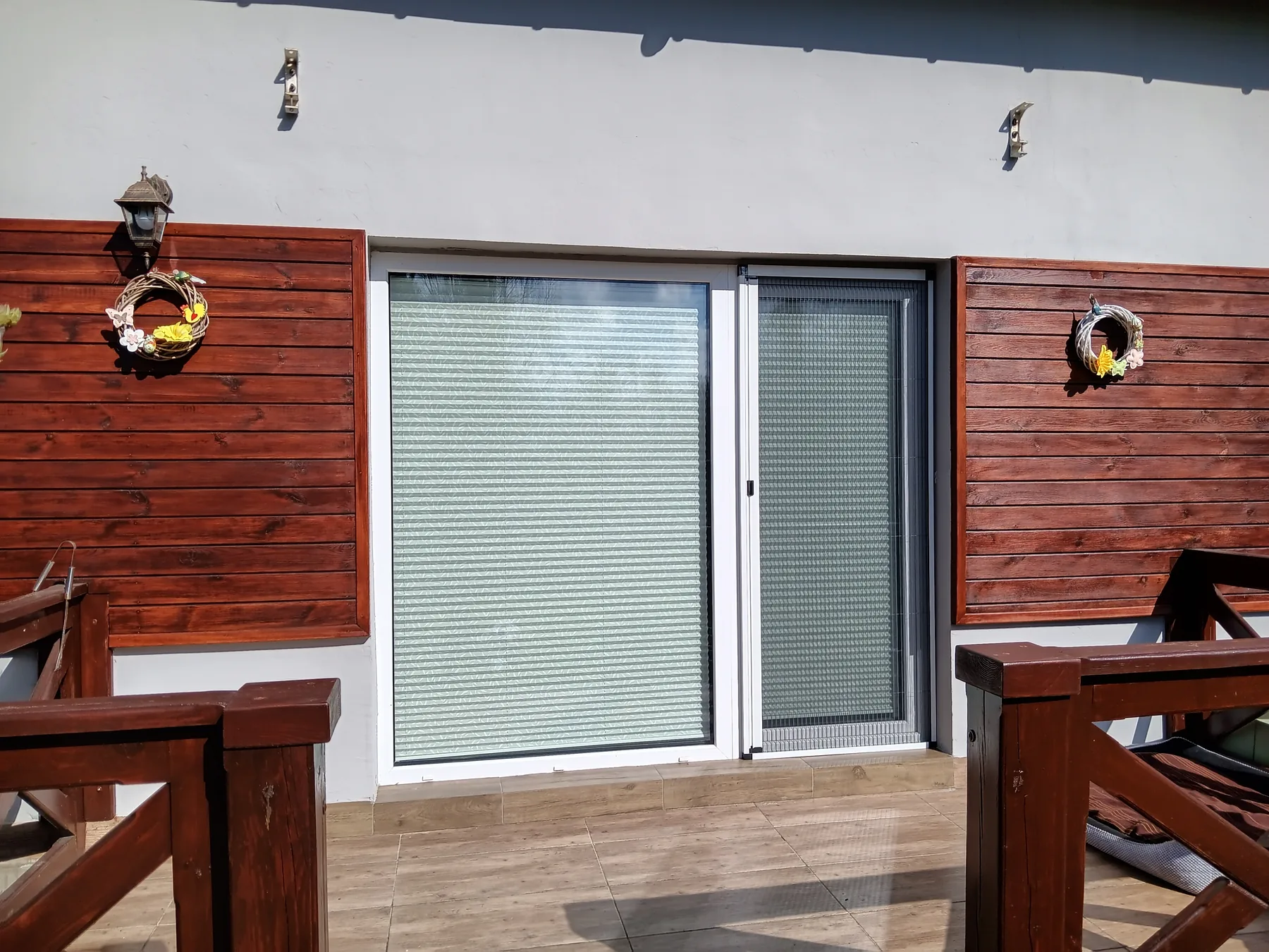 Moskitiera plisowana przy tarasie z drewnianą elewacją w realizacji na Śląsku - widok szerokiego wyjścia tarasowego z moskitierą plisowaną