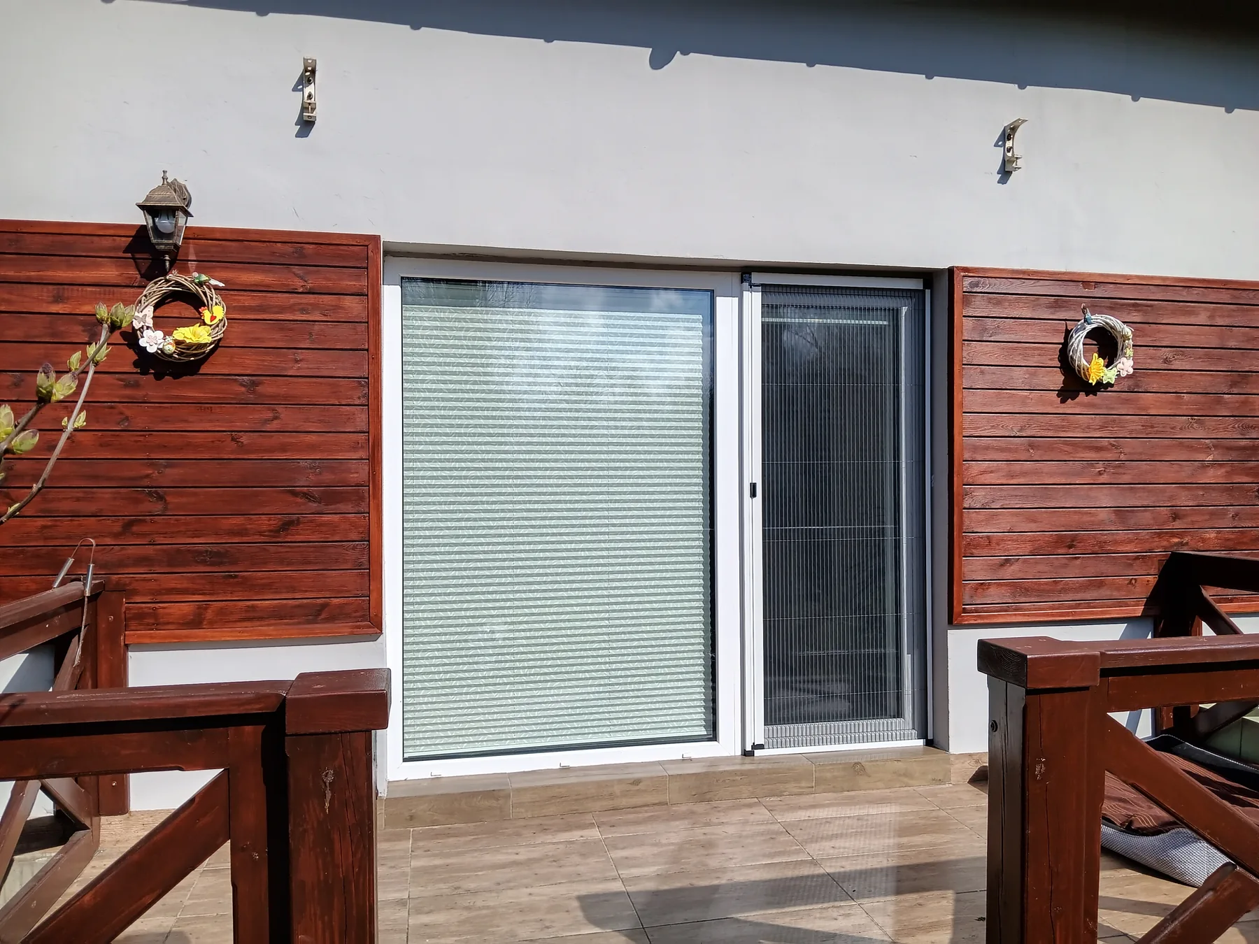 Moskitiera plisowana przy tarasie z drewnianą elewacją w realizacji na Śląsku - kadr pokazujący przejście przy drewnianej elewacji