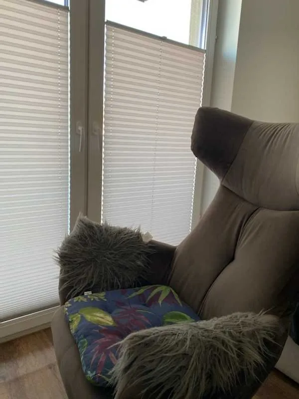 Plisy przy balkonowym przeszkleniu w realizacji na Śląsku - detal tkaniny plisowanej przy fotelu i oknie balkonowym