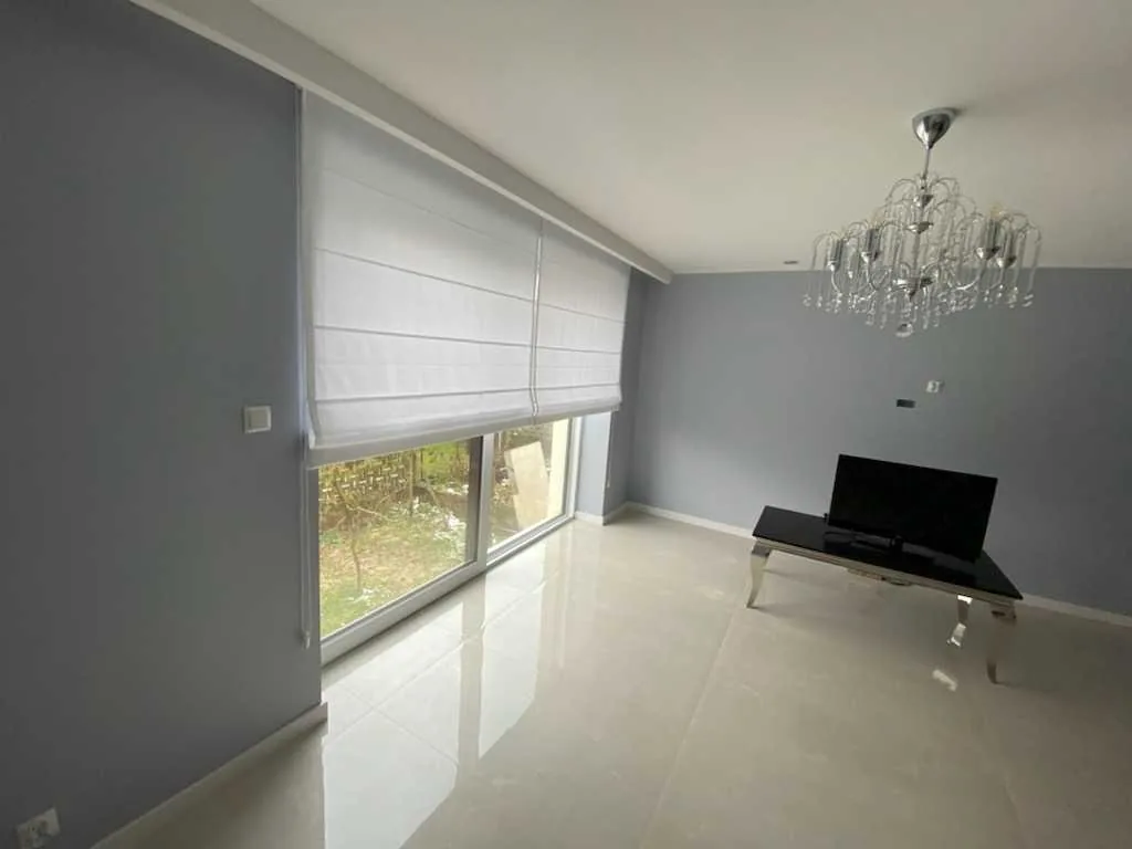 Rolety rzymskie w szarym wnętrzu w realizacji w Bytomiu - kadr dużego przeszklenia z opuszczoną tkaniną