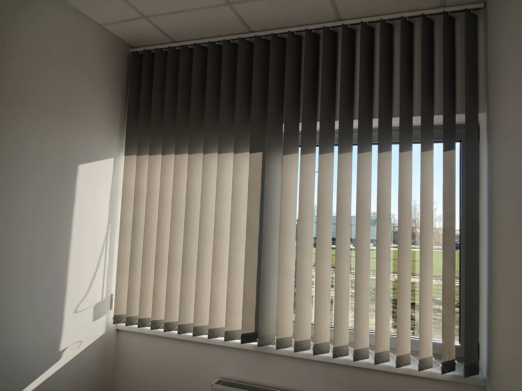 Żaluzje pionowe przy szerokim przeszkleniu w realizacji w Tarnowskich Górach - zbliżenie verticali przy bocznym kadrze okna